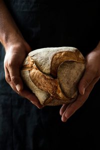 Photographie en clair obscur de pain et de mains, lumière naturelle, recherche personnelle