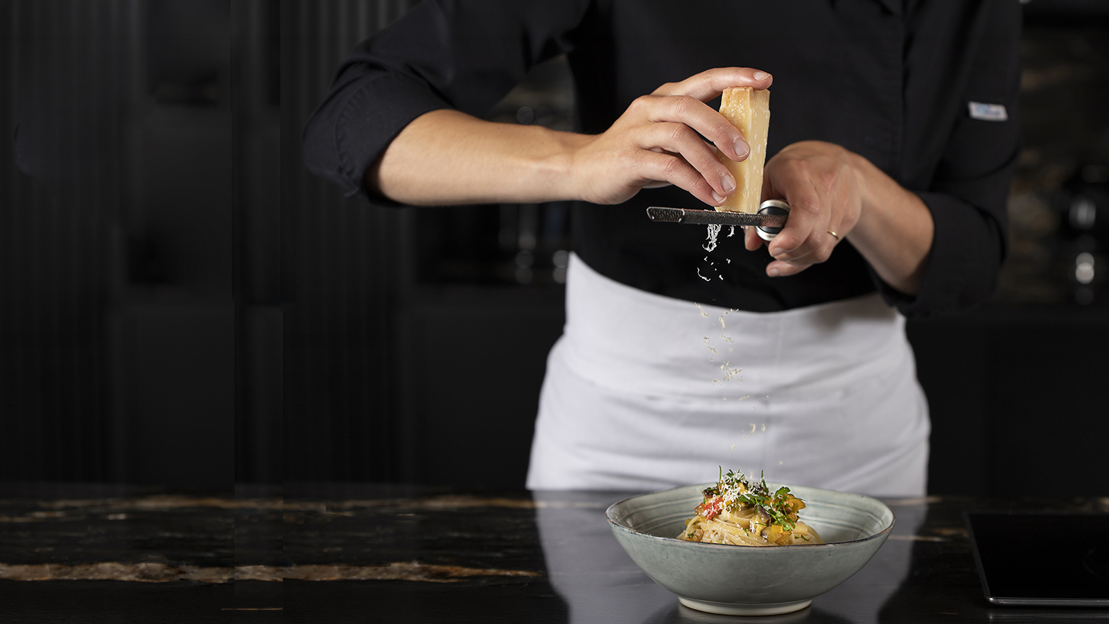Geste en cuisine Cheffe italienne finassant une assiette de pâtes au légumes en la saupoudrant de parmesan