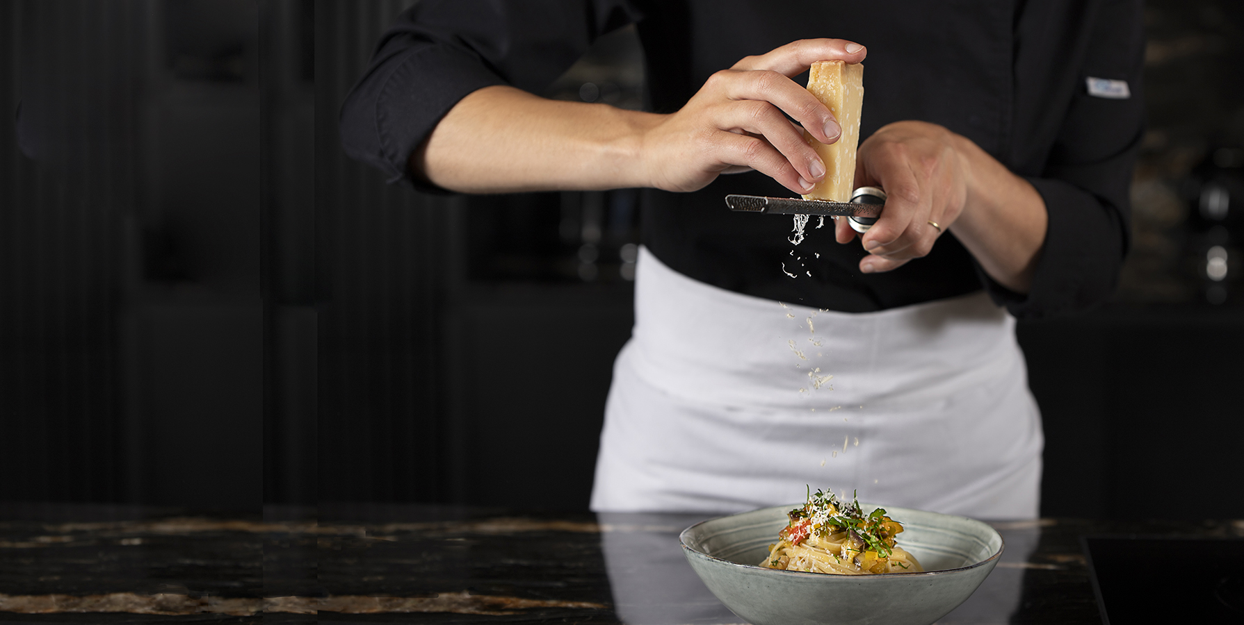 Cheffe saupoudrant une assiette de pâtes de parmesan